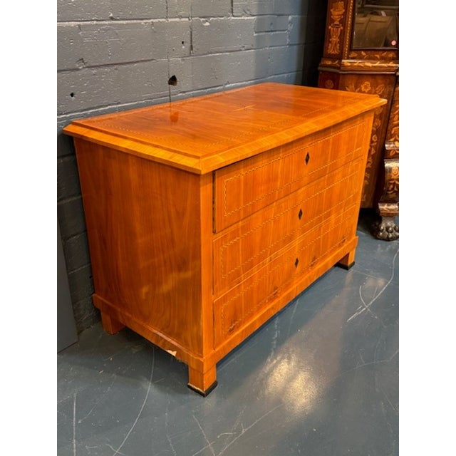 The 19th Century German Biedermeier Fruitwood Commode is an antique chest of drawers that exudes vintage charm and...