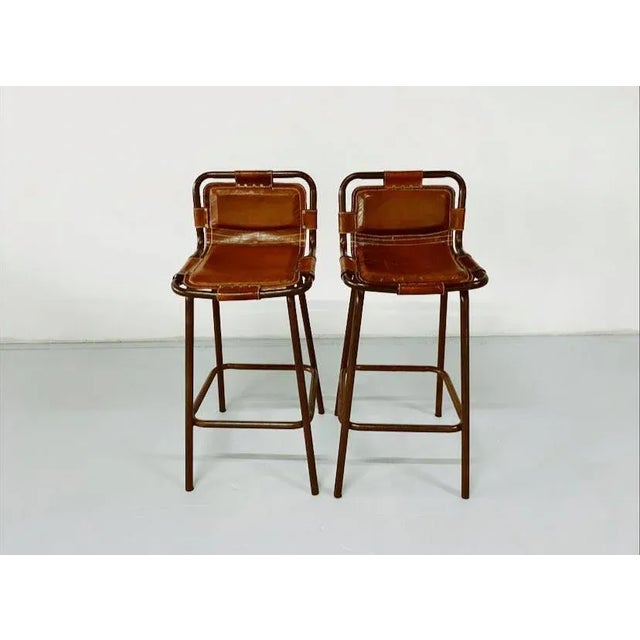 Pair of barstools in the manner of French architect, Charlotte Perriand. Enameled steel & brown leather. France, c. 1960....