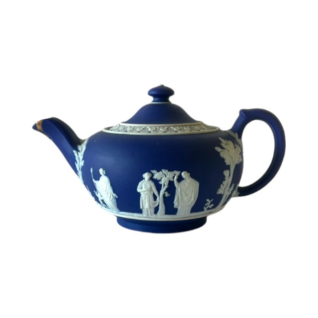 An antique Wedgwood tea pot in deep cobalt blue jasperware with a white relief neoclassical design, and a kintsugi repair...