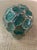 This visually captivating decorative ball possesses a stunning green hue accented by organically shaped ridges in a Nickel...