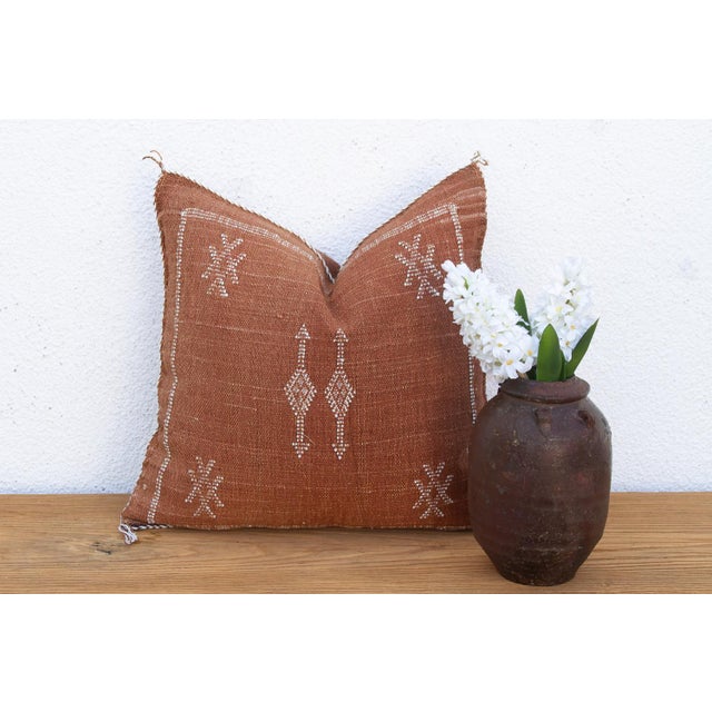 A stacked diamond-and-arrow medallion anchors the center of this handcrafted Moroccan cactus silk pillow, bordered by...