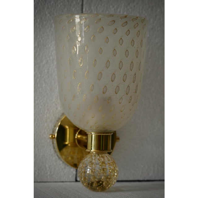 This gold-toned sandblasted Murano glass wall light features a refined and delicate design. The wall light features a...