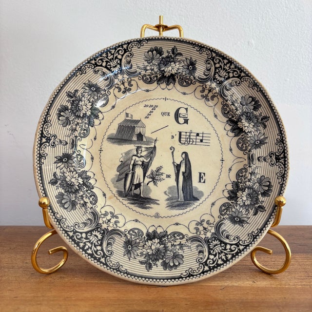 A French rebus puzzle plate, transfer printed in black on a white semi-porcelain body. When solved, the picture puzzle...