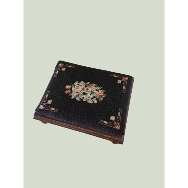 You are viewing an antique footstool with a mahogany wooden base and a cushioned top featuring Victorian needlepoint...