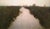 The painting depicts a tranquil waterway meandering through lush, green marshlands, enveloped in a soft, hazy atmosphere....
