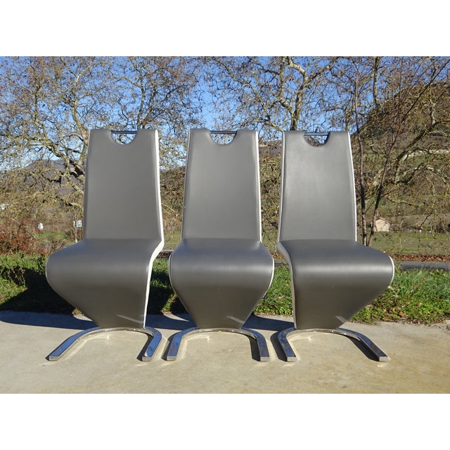 Set of 3 designer chairs, upholstered in grey faux leather with white trim highlighting the Z-shaped profile. High...
