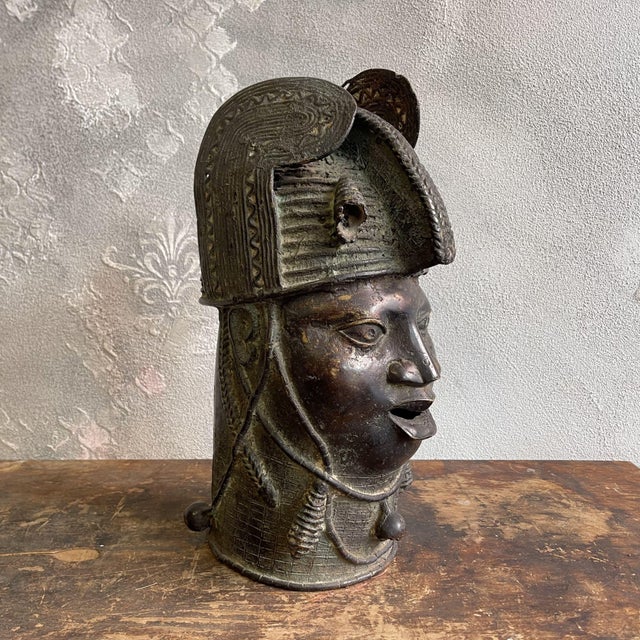 This vintage sculpture depicts the head of a Yoruba Oba, a royal figure from the Kingdom of Benin, created in the 20th...