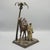 A cold painted and patinated bronze sculpture depicting a bedouin man astride his camel standing under a palm tree....