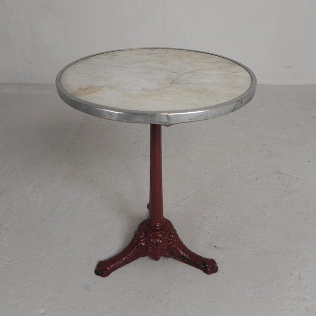 Elegant bistro table from the 1920s with robust cast iron legs and a luxurious marble top. The round marble top rests in...