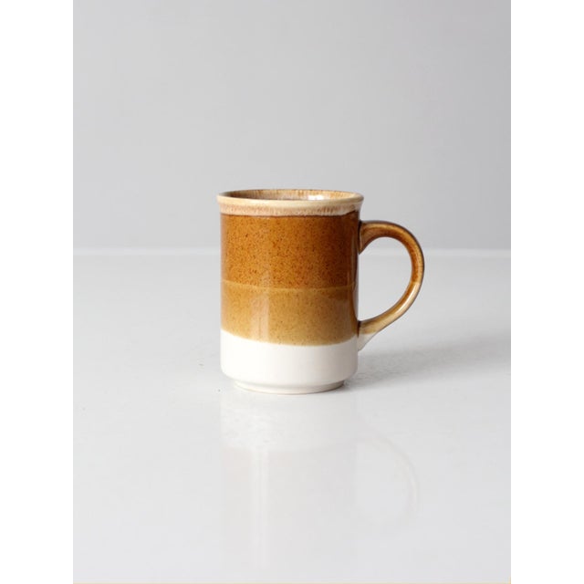 A vintage ceramic coffee mug with warm bands of caramel brown, tan, and cream. The earthy palette and clean cylindrical...