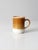 A vintage ceramic coffee mug with warm bands of caramel brown, tan, and cream. The earthy palette and clean cylindrical...