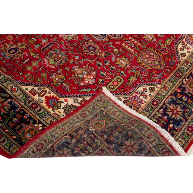 Beautiful vintage Persian Tabriz hand-knotted wool rug with a red color field. This piece has a navy blue frame and...