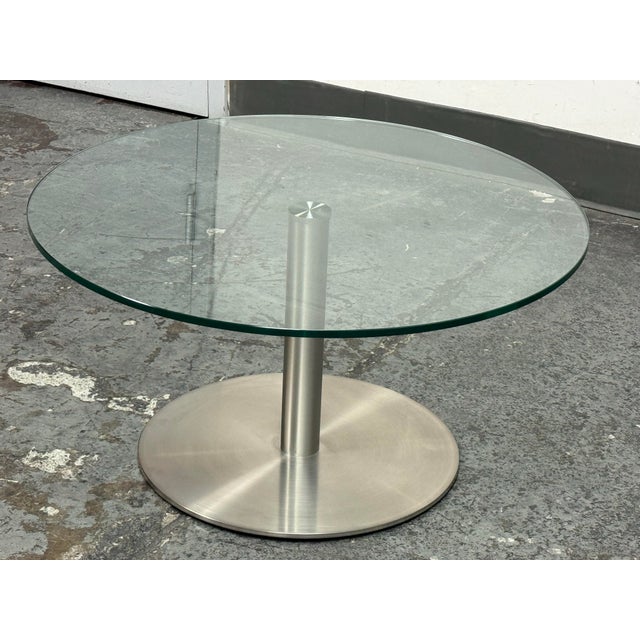 Design Plus Gallery presents the Berta Coffee Table by Scandinavian Design. A round glass top rests on a cylindrical metal...