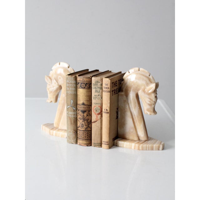 This striking pair of vintage Art Deco bookends is carved from banded onyx, featuring stylized horse heads with a forward-...