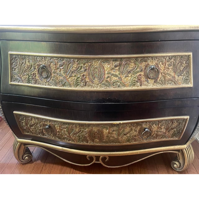 Striking bombe-form two-drawer chest with ebonized finish, gold-leaf trim, nailhead detailing, and richly embossed floral...