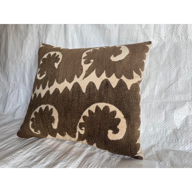 A striking decorative pillow fashioned from an early 1900s hand-embroidered Suzani textile, featuring a bold large-scale...