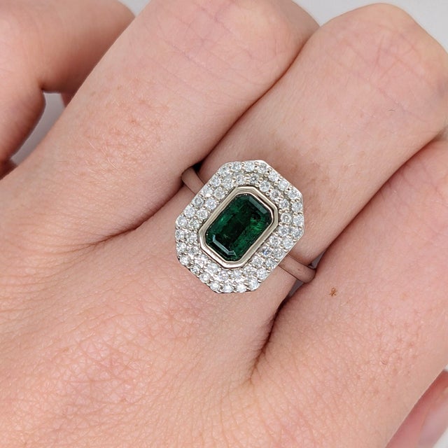 A Zambian emerald rests in a lush, forest green at the centre of this solid 14K white gold ring, encircled by fifty earth-...
