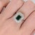 A Zambian emerald rests in a lush, forest green at the centre of this solid 14K white gold ring, encircled by fifty earth-...