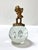 A gold-tone cherub playing a lyre sits atop a clear glass orb with three suspended teardrop-shaped bubbles. A decorative...