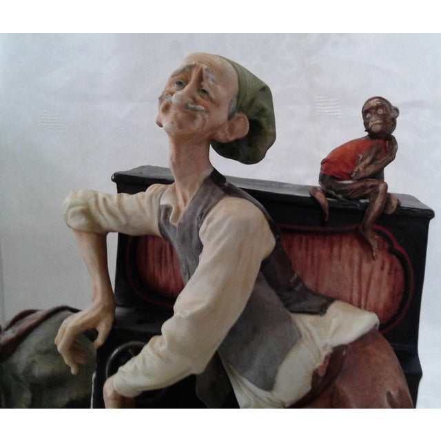 A detailed, hand-painted Italian polychrome porcelain figurine group depicting an elderly street musician/organ grinder...