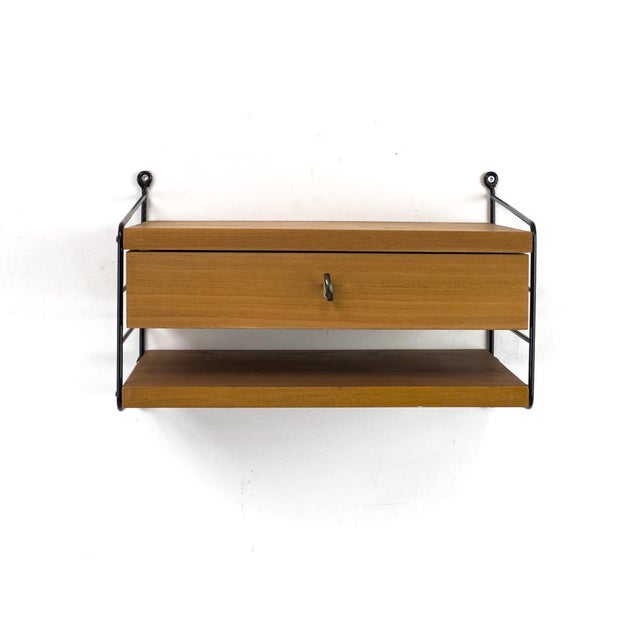 Original String shelving system consisting of two black ladders (28 cm deep, 26 cm high), a shelf, and a drawer unit....