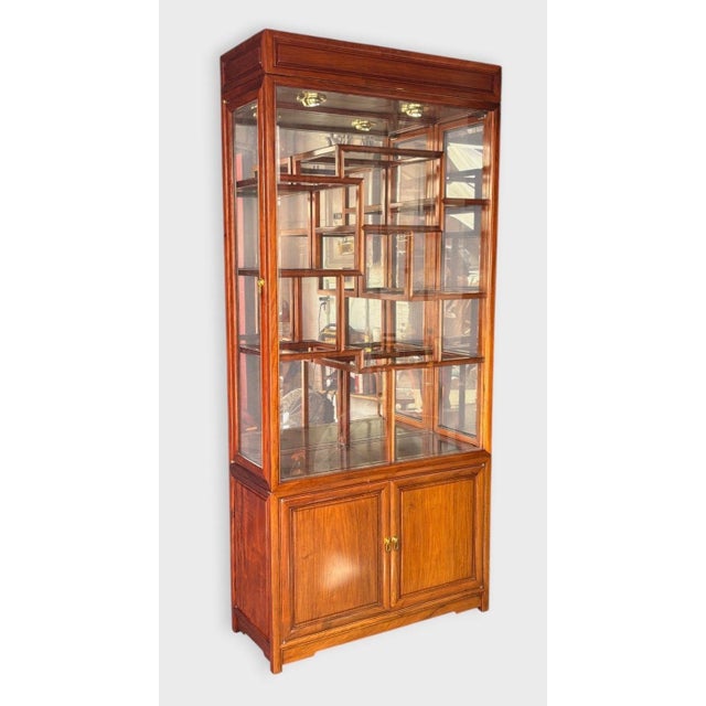 Tall Asian-or Chinoiserie-style display cabinet with a warm rosewood finish, glazed front and side panels, interior...