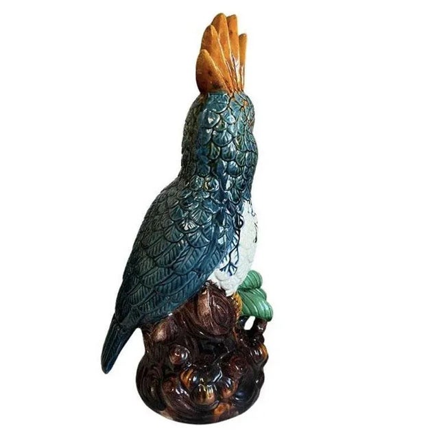 A tall bright ceramic bird sculpture in the style of Meissen. Glazed in blue, green, orange and brown polychrome, this...
