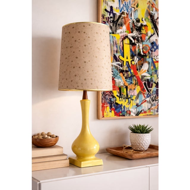 Vintage Mid Century Modern table lamp featuring a glossy yellow ceramic base with a sculptural silhouette and a warm...