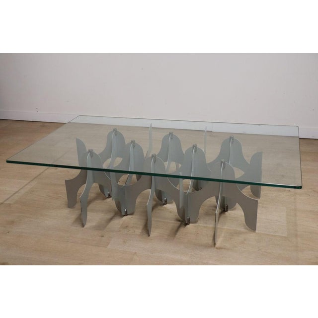 Sculptural coffee table with a minimalist 80s design. Structure in superimposed metal slats and thick transparent glass...