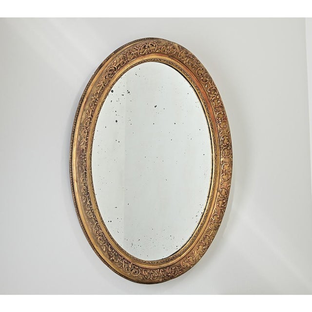 A opulent and intricately carved French 19th Century Napoleon III style giltwood oval mirror that will instantly transform...