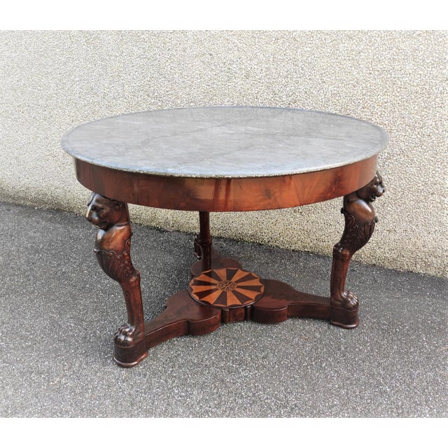 Round mahogany table featuring three lion-shaped carved uprights, joined at the base by an inlaid top. Contemporary gray...