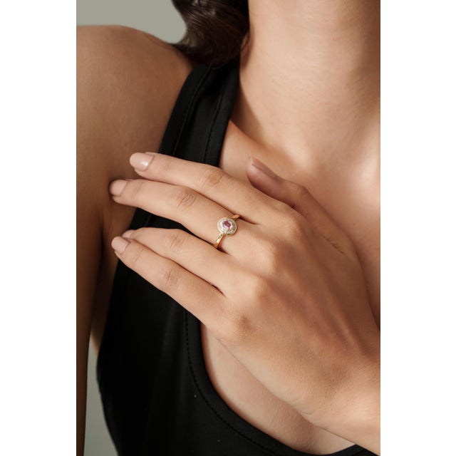 This halo ring is featuring a 0.3 ct oval pink sapphire set in 14K yellow gold. The sapphire measuring 4 x 5 mm as the...