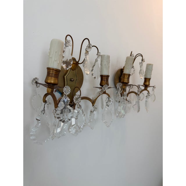 Elegant vintage brass and crystal two-light wall sconces featuring gracefully curved arms adorned with faceted crystal...