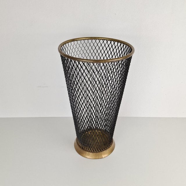 This umbrella stand, designed in the style of Mathieu Matégot in the 1950s, features a black metal mesh frame and a gold-...