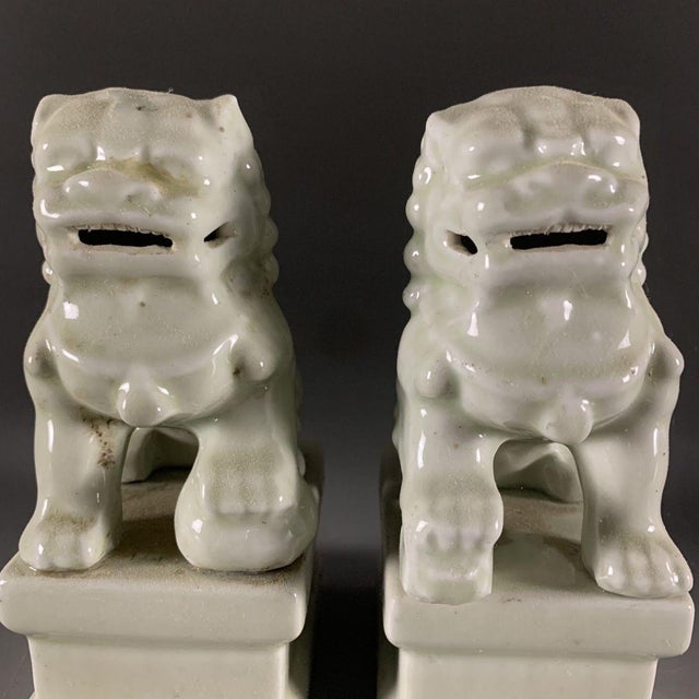 This charming matching pair of Chinese foo dogs (guardian lions) is crafted from porcelain finished in a soft pale celadon...