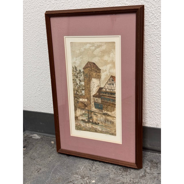 Design Plus Gallery presents the “Weinstadel" Framed Etching by M. Leianne. This hand-colored etching depicts a canal-side...