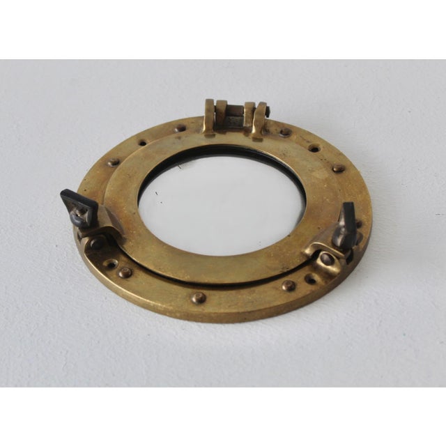 Vintage brass nautical porthole mirror with a heavy metal frame, functional hinge, and swing-bolt closures. Just 7.25" in...