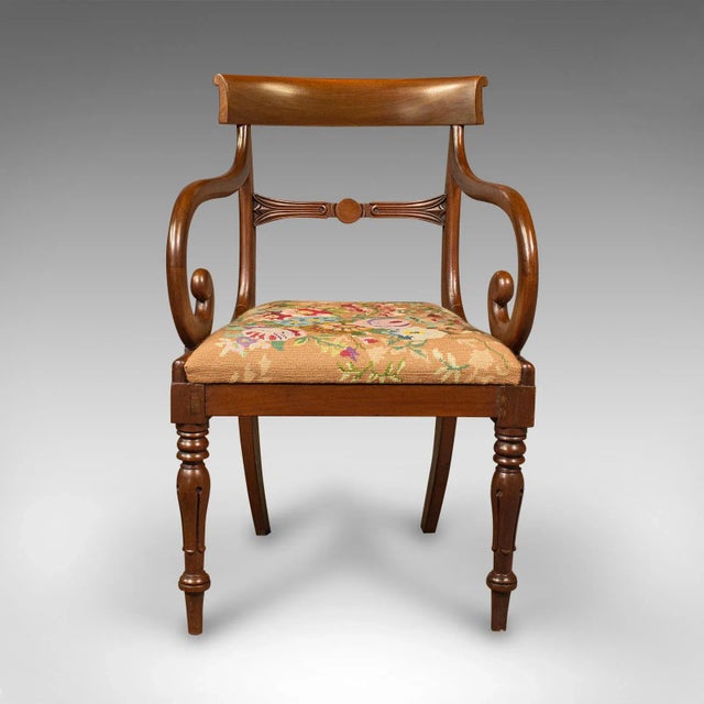 This is an antique scroll arm chair. An English, mahogany armchair with needlepoint upholstery, dating to the Regency...