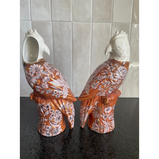 This is a pair of identical glazed ceramic vases, in the shape of a cockatoo. White with ocher and pink decorative decals.