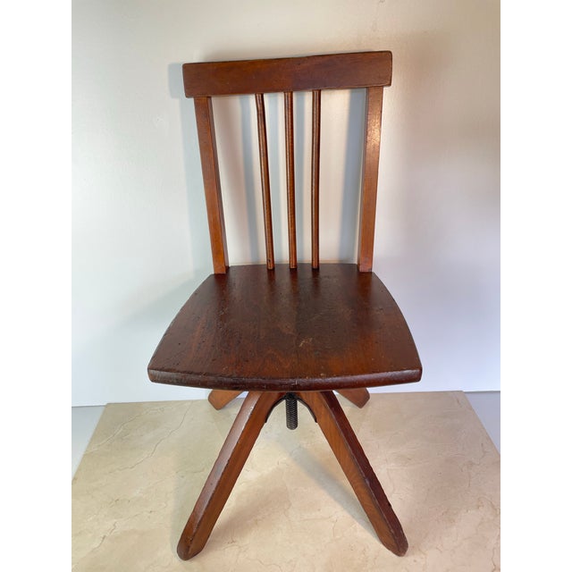 A charming vintage rustic industrial child's swivel chair featuring solid hardwood construction paired with durable cast...