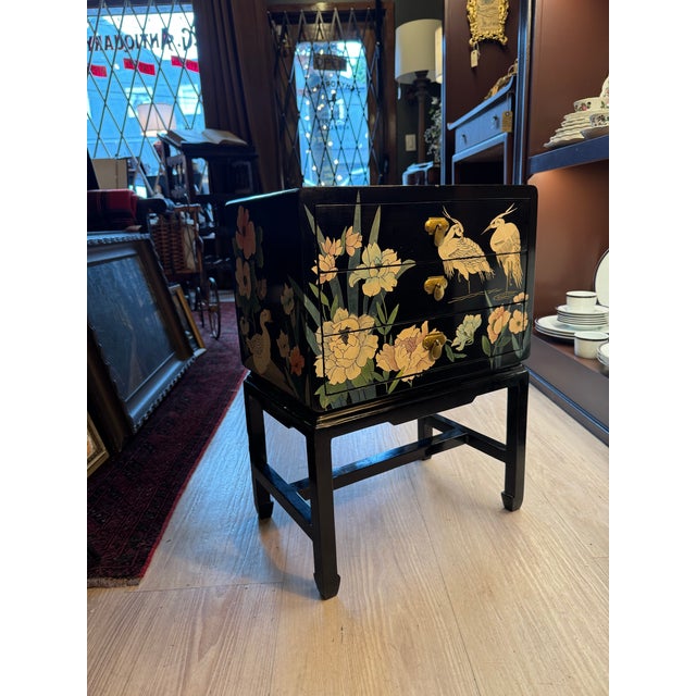 A beautifully decorated vintage lacquered chest featuring delicate bird and floral scenes rendered in soft pale pinks,...