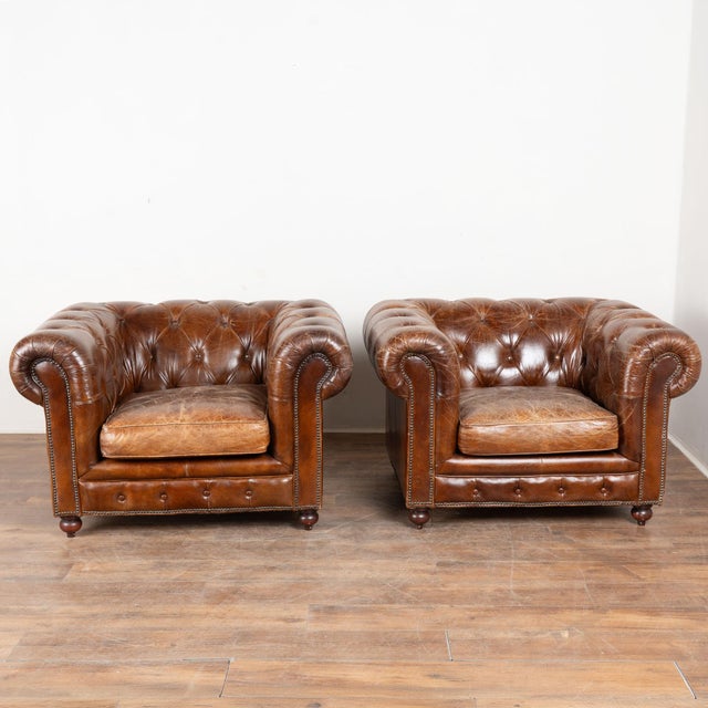 Pair of 20th century English Chesterfield club chairs upholstered in vintage brown leather. Traditional button tufted...