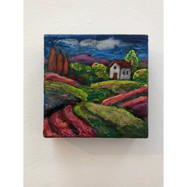 This encaustic work on wood block presents a vibrant landscape, featuring rolling hills adorned with lush greenery and a...