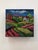 This encaustic work on wood block presents a vibrant landscape, featuring rolling hills adorned with lush greenery and a...