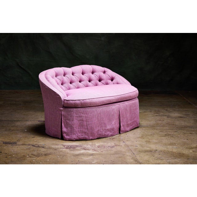 Petite Skirted Loveseat vintage upholstered loveseat in pink striped fabric with a button-tufted kidney-shaped back. This...