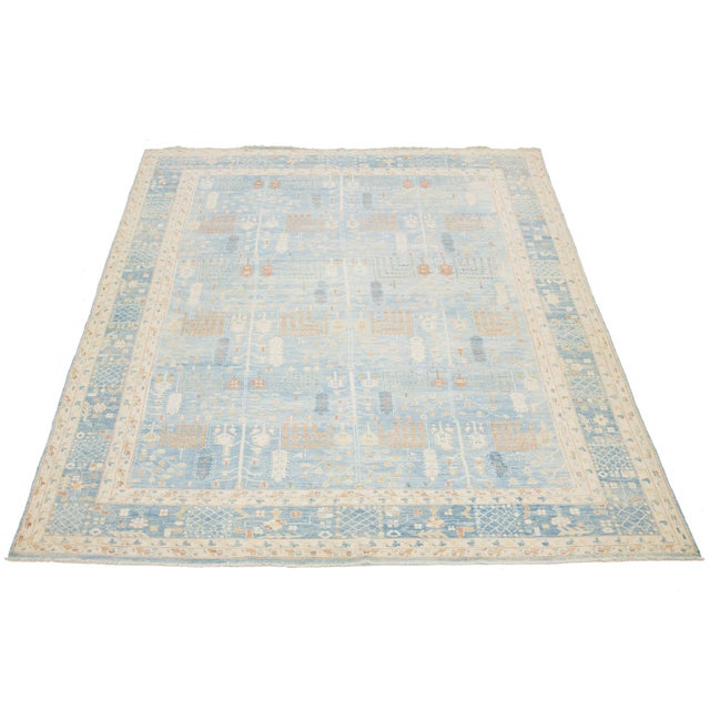 This stunning modern Khotan hand-knotted wool rug showcases a serene light blue background, beautifully framed by an...