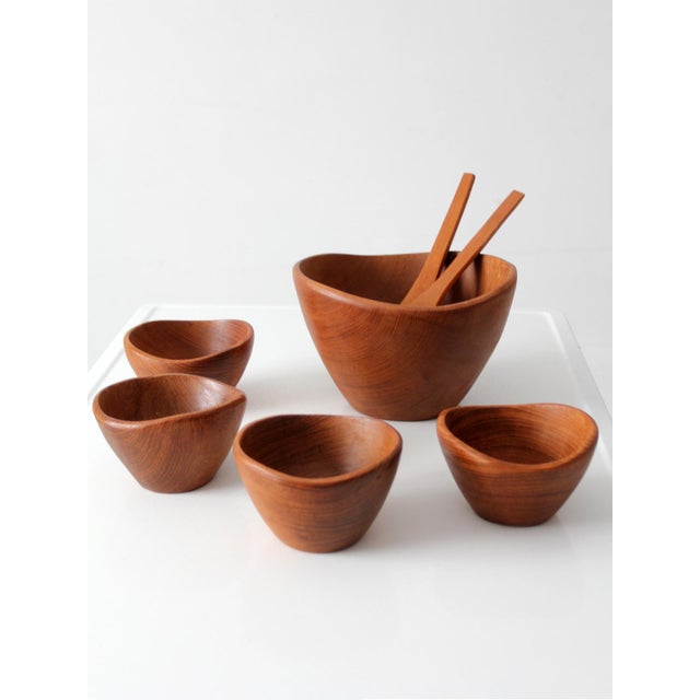 A vintage mid-century teak salad bowl set comprising a large sculptural serving bowl, four individual bowls, and a...