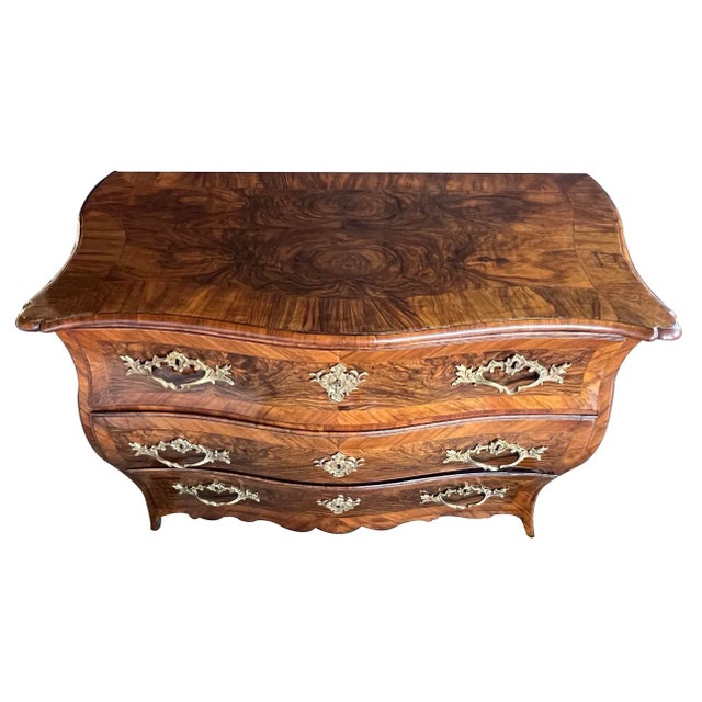 the serpentine top above a bombe-form body fitted with three drawers adorned with bold bronze foliate mounts; all in a...