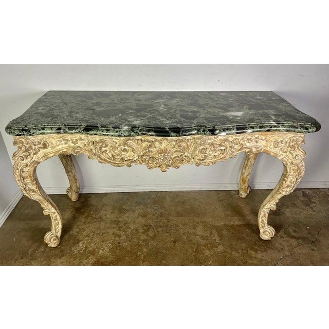 French carved Louis XV style console in a distressed painted finish. The marble top is 2" thick in a soft green...