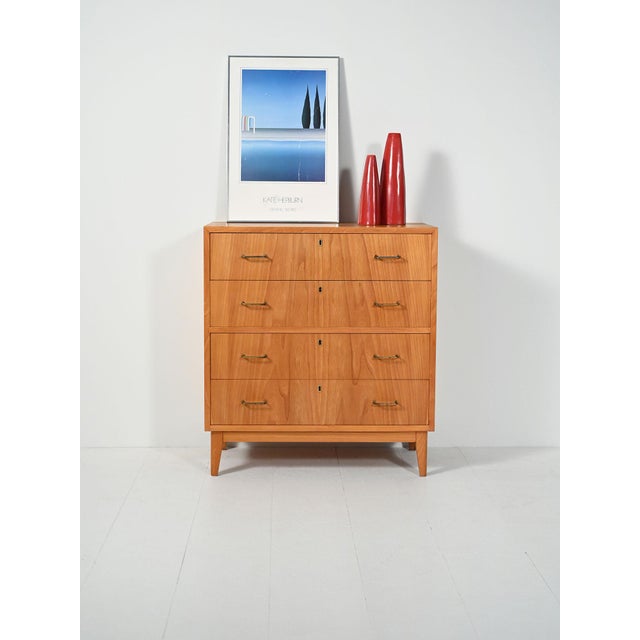 Elm chest of drawers with four spacious drawers, contrasting brass handles, and slightly flared legs. Warm finish,...